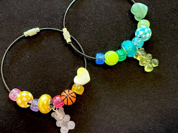 Two bracelets on black fabric strung with Phoenix Challenge beads, among them checkerboard, heart, basketball and tennis ball beads and a gummy bear charm.